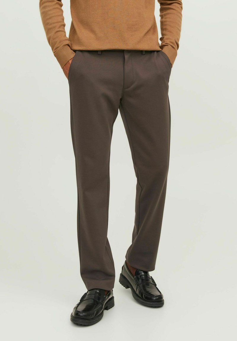 Pantalones marrones a medida con una textura suave y un diseño clásico. Presenta bolsillos laterales y un corte de pierna recta. Llevado con mocasines negros.