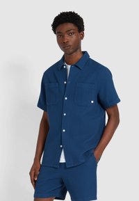 Kurzärmeliges, strukturiertes Hemd in Marineblau mit zwei Brusttaschen und Knopfleiste, kombiniert mit passenden Shorts. Leicht und lässig geschnitten.
