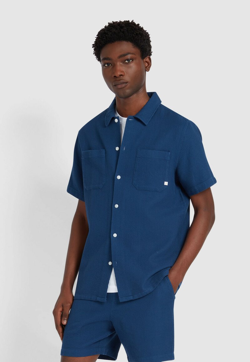 Kurzärmeliges, strukturiertes Hemd in Marineblau mit zwei Brusttaschen und Knopfleiste, kombiniert mit passenden Shorts. Leicht und lässig geschnitten.