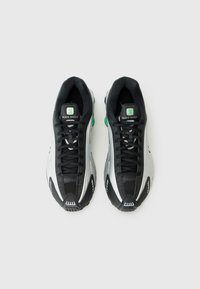 Fekete és ezüst sportcipők, hálós felsőrésszel, figyelemfelkeltő zöld kiegészítőkkel, texturált gumitalppal és fűzős kialakítással. Nike Shox márkajelzéssel rendelkezik.