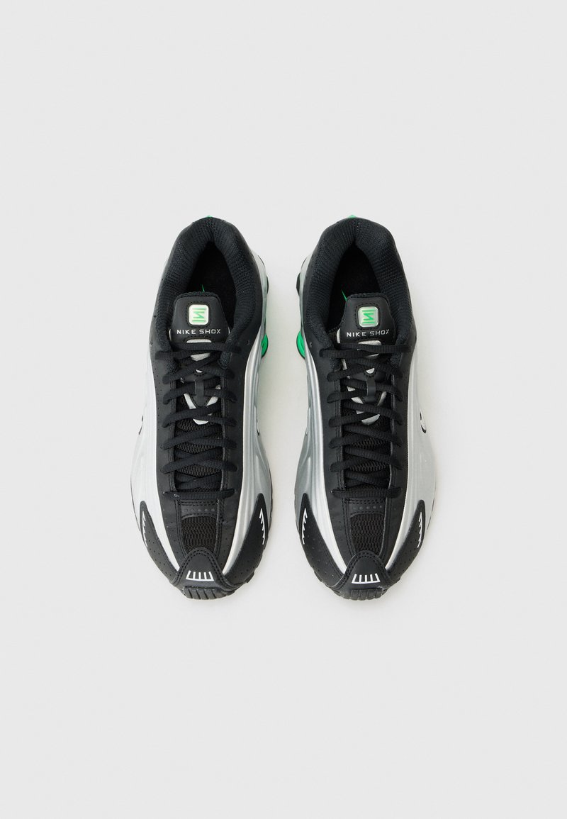 Baskets de sport noires et argentées avec tige en mesh, accents verts frappants, semelle en caoutchouc texturé et design à lacets. Présente le logo Nike Shox.