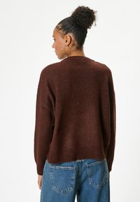 Maglione marrone lavorato a maglia con una vestibilità rilassata, colletto e orlo a coste, abbinato a jeans blu a vita alta. Texture morbida con un leggero dettaglio scintillante.