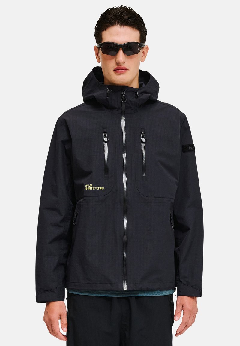 Sort vandtæt jakke med hætte, frontlynlås og reflekterende detaljer. Har to lynlås lommer og tekstaccenter i gul.