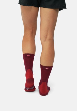 Burgundy-sukat ribattavilla varrella, kontrastoivilla kantapää- ja varvasalueilla. Varressa logo ja pinnallinen pohja pitävyyttä varten. Pehmeä neulemateriaali.