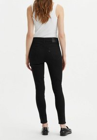 Svarta skinny jeans med högmidjad passform, med en slät denimtextur, subtil sömnad och två bakfickor, bärs med en vit linne.