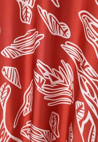 Tissu rouge avec une finition satinée présentant des motifs de feuilles et de lignes blanches, mettant en valeur une texture lisse et des éléments de design fluides.