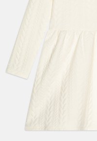 Sukienka w kolorze kremowym wykonana z fakturowanej tkaniny z wzorem warkoczowego splotu, z długimi rękawami i rozkloszowaną spódnicą.