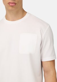 T-shirt bianco in cotone con scollo rotondo e taschino sul lato sinistro del petto. Il tessuto ha una texture liscia e una vestibilità casual.