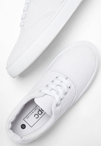 Sneakers in tela bianchi con una superficie morbida, punta rotonda, suola in gomma e sei occhielli per i lacci. L'etichetta interna mostra la taglia 37.