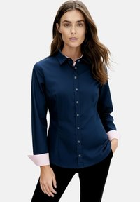 Navy blue button-up shirt with long sleeves, featuring light pink striped cuffs and collar accents. Smooth fabric with a tailored fit.