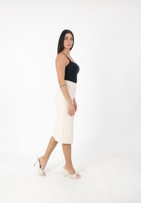 Schwarzes Spaghettiträgershirt, cremefarbener Midirock und gemusterte, offene Sandalen mit goldenen Akzenten. Das Model steht seitlich und hebt die Formen des Outfits hervor.