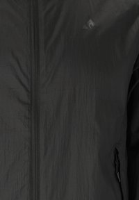 Sort let jakke med frontlynlås og lille brystlogo på struktureret stof.