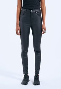 Jeans skinny in ecopelle nera con vita alta, chiusura a zip e bottone, tasche anteriori e posteriori, caratterizzati da una texture liscia e raffinata.