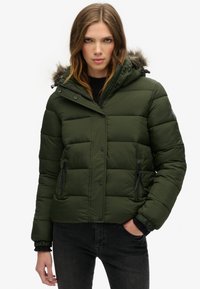 Veste matelassée verte avec capuche, dotée d'une bordure en fourrure, de boutons-pression à l'avant et de poches zippées. Design texturé et matelassé avec des manches côtelées.