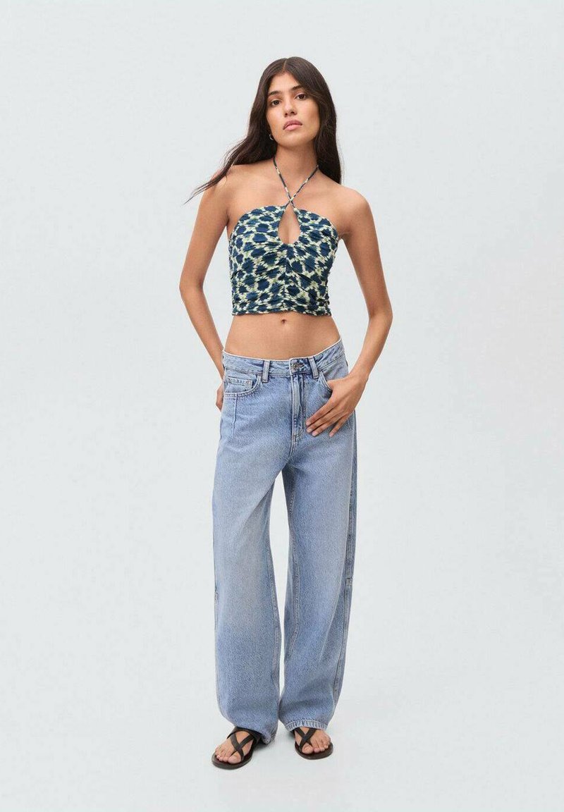 Modrá vzorovaná halter crop top s detailom v tvare kľúčovej dierky, spárovaná s voľnými svetlomodrými džínsami a čiernymi žabkami.