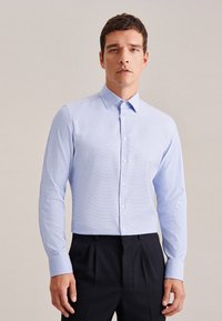 Camicia button-up azzurro chiaro, maniche lunghe, in cotone con una leggera texture, colletto classico, abbinata a pantaloni scuri. Nessun motivo o accento visibile.