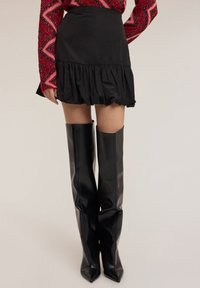 Minifalda negra con dobladillo con volantes, confeccionada en tela ligera. Combinada con botas negras de cuero hasta la rodilla con diseño de punta afilada.