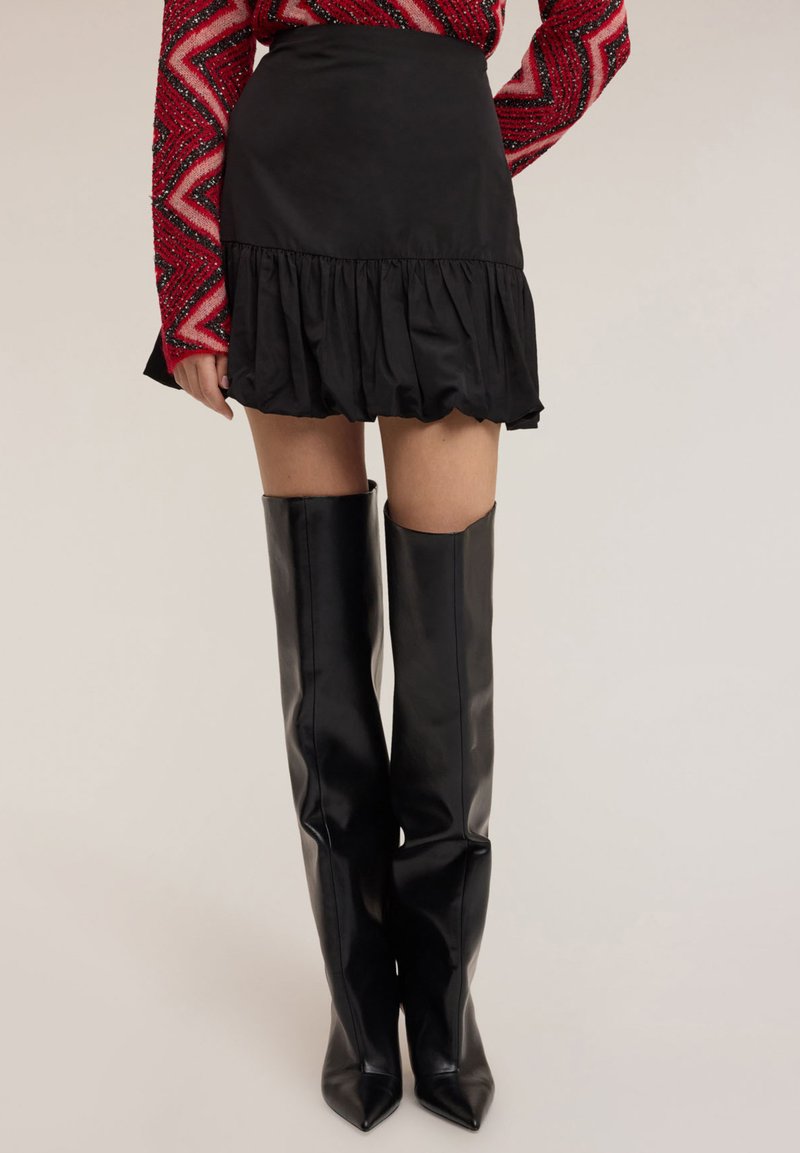 Minifalda negra con dobladillo con volantes, confeccionada en tela ligera. Combinada con botas negras de cuero hasta la rodilla con diseño de punta afilada.