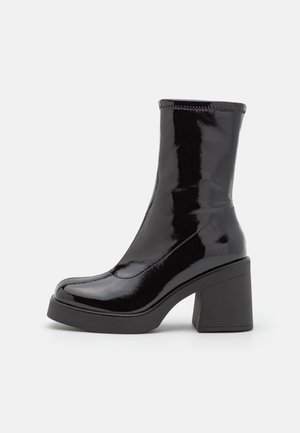 Shiny black ankle boot with a rounded toe, thick block heel, and smooth, high-gloss finish on a plain background.