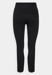 Jean skinny noir taille haute vu de dos avec deux poches arrière et une petite étiquette blanche sur la poche droite.