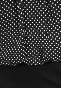 Černá tkanina s bílými puntíky přehnutá přes jednobarevnou černou tkaninu, ukazující texturu a záhyby.