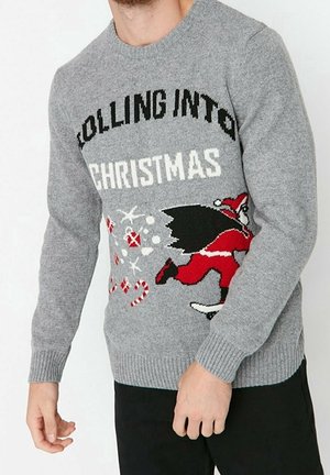 Uomo che indossa un maglione di Natale grigio con Babbo Natale che corre, bastoncini di zucchero, ornamenti e la scritta "Rolling into Christmas".
