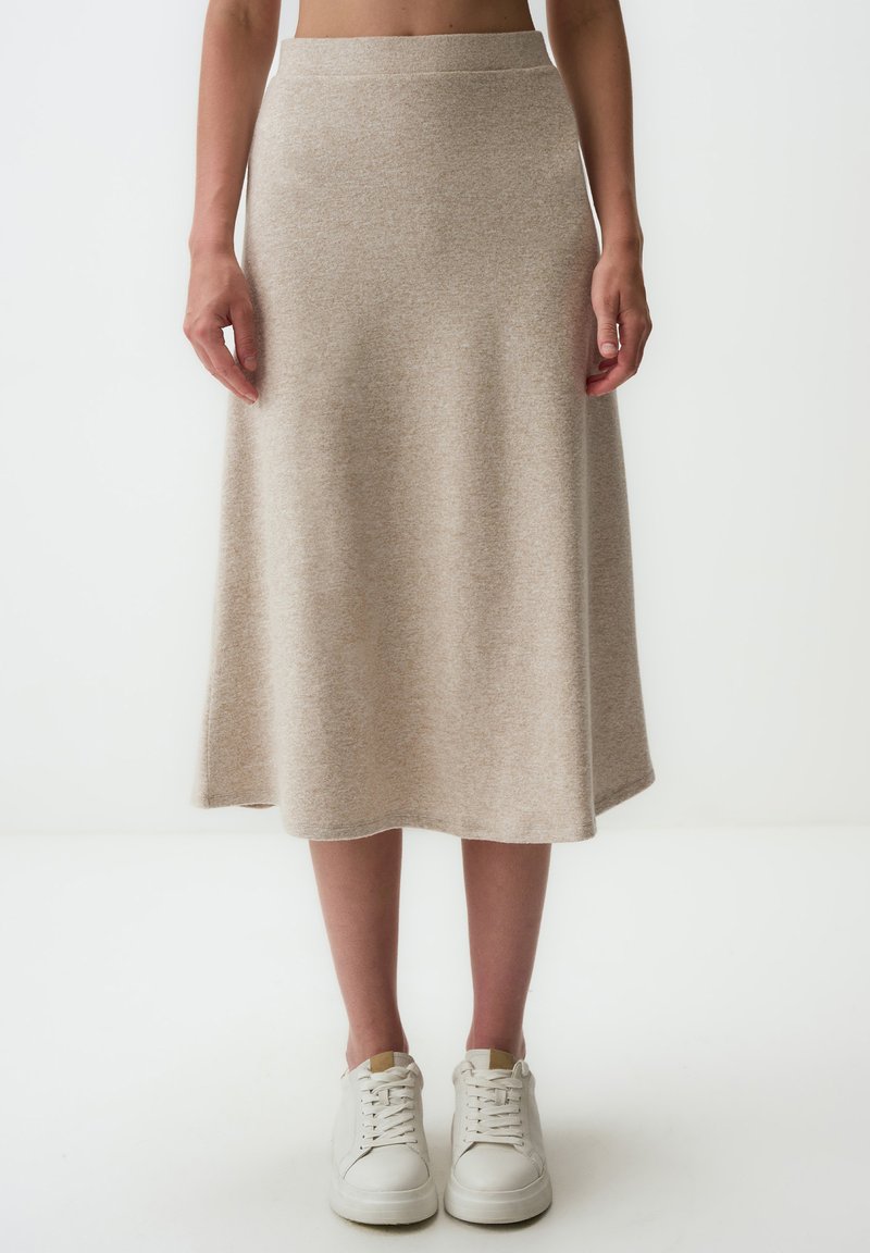Jupe midi en maille beige avec une texture lisse, une silhouette évasée et une taille élastique, associée à des baskets blanches.