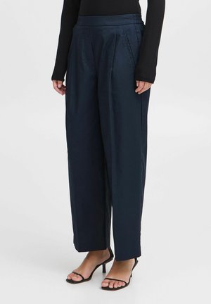 Navybroek met wijde pijpen van soepel materiaal; voorzien van plooien, een hoge tailleband en zijzakken; gecombineerd met zwarte sandalen met bandjes.