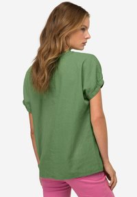 Camicetta verde a maniche corte con una vestibilità rilassata, realizzata in tessuto leggero; presenta risvolti sulle maniche e un orlo dritto.