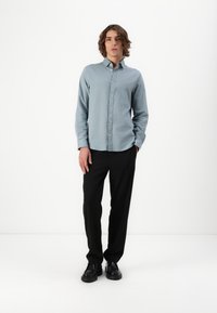 Hellblaues Hemd mit Kragen, kombiniert mit einer schwarzen Hose und schwarzen Schuhen. Das Hemd hat eine strukturierte Oberflächenbeschaffenheit.