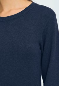 Marinblå stickad tröja med ribbat runt halsen och långa ärmar i en mjuk textur. Inga synliga mönster eller detaljer.
