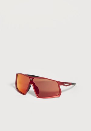 Lunettes de sport rouges avec monture métallique angulaire et verres miroir orange, reposant sur une surface blanche.