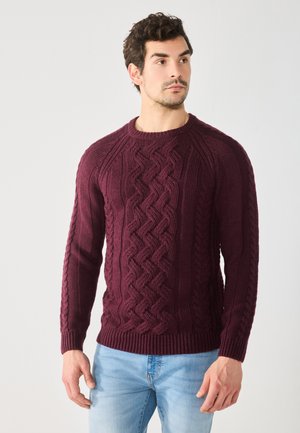 Pull en cuir bordeaux avec un motif en relief, col rond, poignets et ourlet côtelés, associé à un jean en denim bleu clair.