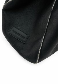 Sac en cuir noir avec une surface texturée, présentant une couture visible et une étiquette rectangulaire embossée avec "FREDSBRUDER".