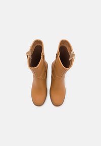 Botines de cuero marrón claro con una textura suave, cremalleras laterales y una lengüeta en la parte posterior, que presentan una puntera redondeada y detalles de costura.
