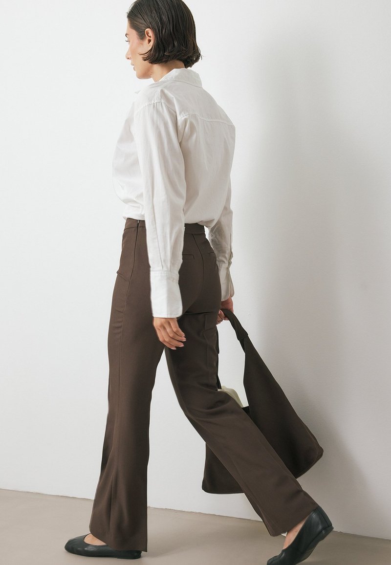 Witte langemouwen shirt, bruine flared broek, zwarte ballerina's en bruine tas. Glad stof, gestructureerd ontwerp, neutrale kleuren en rechte lijnen.