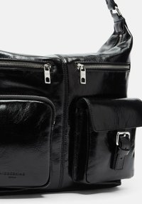 Czarna skórzana torebka z wieloma zamykanymi na zamek przegrodami, frontową kieszenią oraz paskiem z klamrą. Gładka, błyszcząca tekstura.