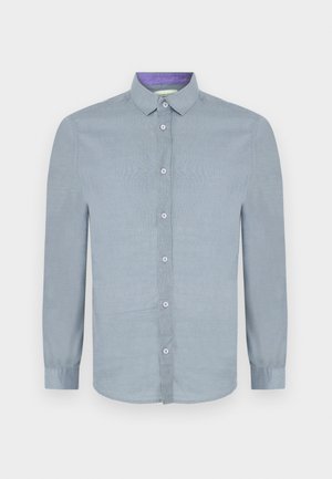 Camisa de manga larga azul claro con cuello abotonado, botones en el frente y una textura suave. El interior del collar presenta un acento púrpura en contraste.