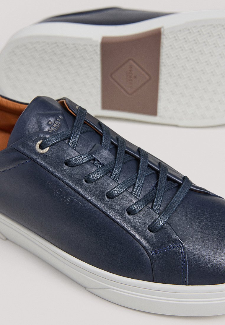 Baskets en cuir bleu marine au texture lisse, avec une semelle en caoutchouc blanc, des lacets assortis et un logo en relief sur le côté.