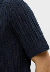 Tenger�észkék, kötött, rövid ujjú felső, amely textúrázott, nyitott mintával rendelkezik, függőleges csíkokkal és bordázott mandzsettákkal.