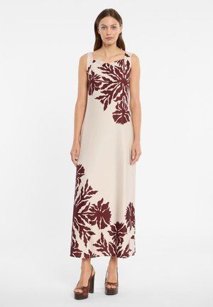 Frau steht in einem ärmellosen beigen Maxikleid mit großen dunkelroten Blumenmustern, trägt braune Plateau-Absatzschuhe, vor weißem Hintergrund.