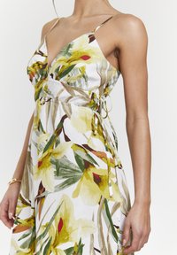 Vestido floral con flores amarillas y verdes sobre una tela blanca. Tirantes finos con lazo ajustable, ligero fruncido en la cintura.