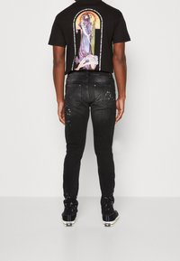 Musta denimfarkut, slim fit -leikkauksella, joissa kulutettuja yksityiskohtia ja ompeleita. Yhdistetty mustaan graafiseen t-paitaan, jossa on värikäs kuvitus.