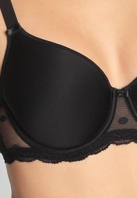 Sujetador negro con copas acolchadas, lados de malla transparente con puntos y encaje en la parte inferior. Tirantes ajustables, textura suave.