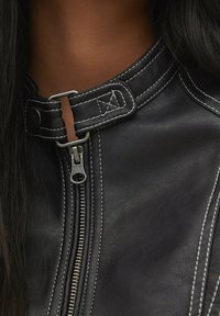Black leather jacket featuring a high collar, silver hardware zip closure, contrasting white stitching, and detailed stitching accents.