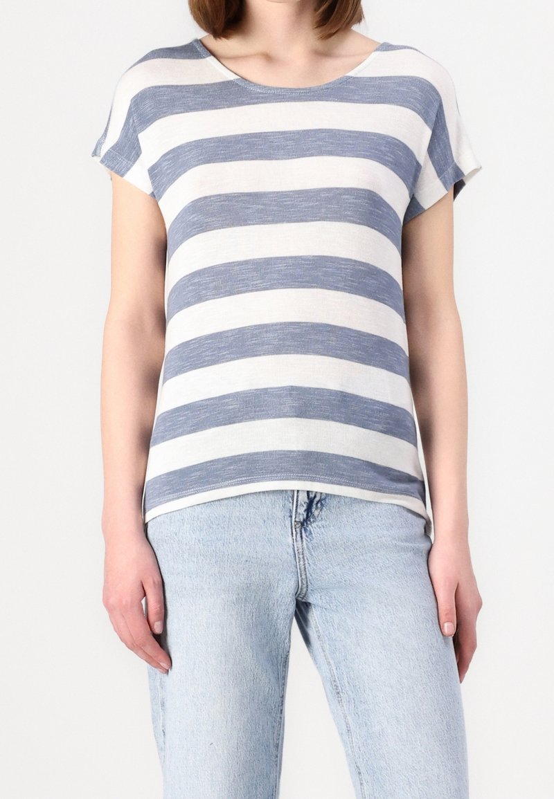 Pruhované tričko ve světle béžové a námořnické modré, vyrobené z měkké tkaniny, s kulatým výstřihem a krátkými rukávy, nošené se světle modrými džíny.