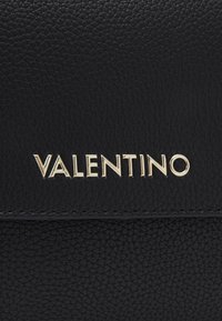 Černá kožená kabelka s texturovaným povrchem a zlatým logem "VALENTINO" pro embossované na přední straně. Minimalistický design bez dalších dekorací.