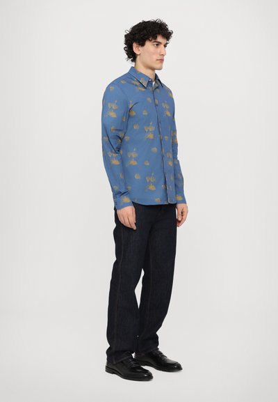 Camisa de manga larga azul con patrón floral dorado, cuello abotonado y textura suave, combinada con jeans de mezclilla oscura y zapatos negros.