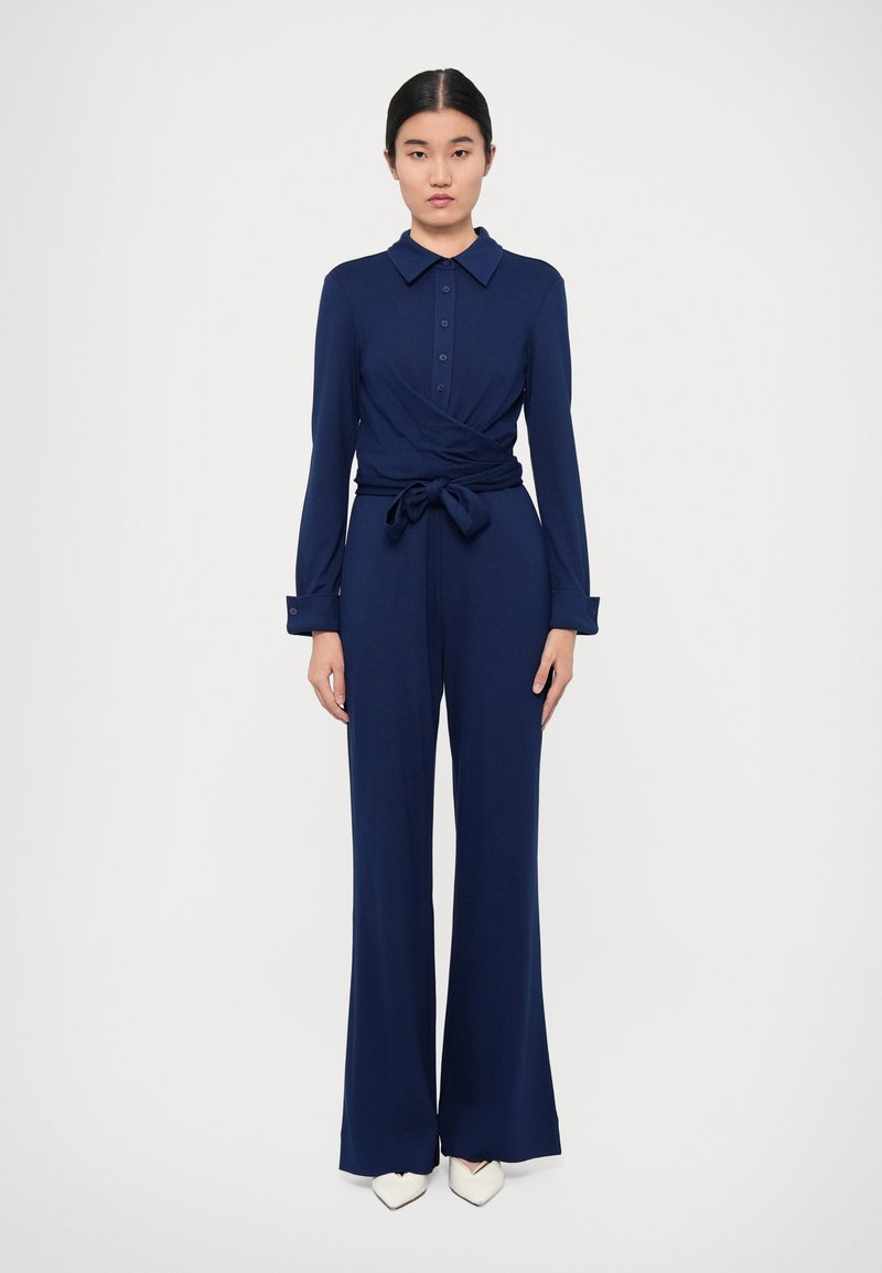 Marineblauw jumpsuit met een wikkelontwerp, kraag, knopenfront, lange mouwen en een gestrikt middel. Kenmerken zijn wijde broekspijpen en een gladde textuur.