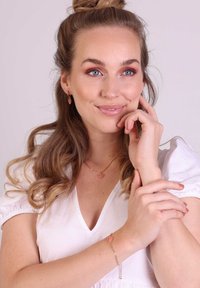 Gouden sieraden met een hartpendant aan een kettinghalsketting en bijpassende oorbellen, beide met een roze edelsteen detail.